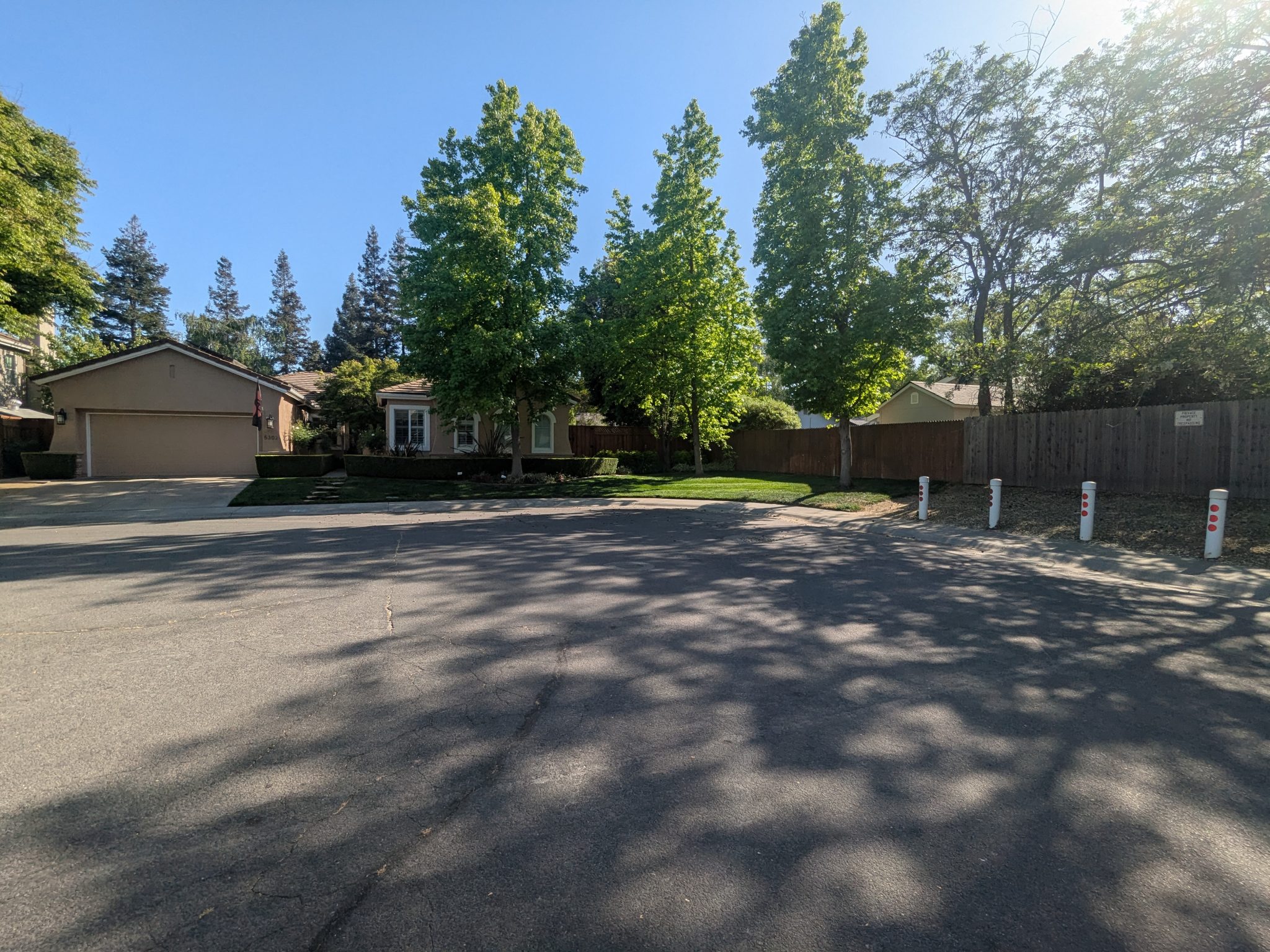 Suburban house with trees in cul de sac with white posts in front of fence