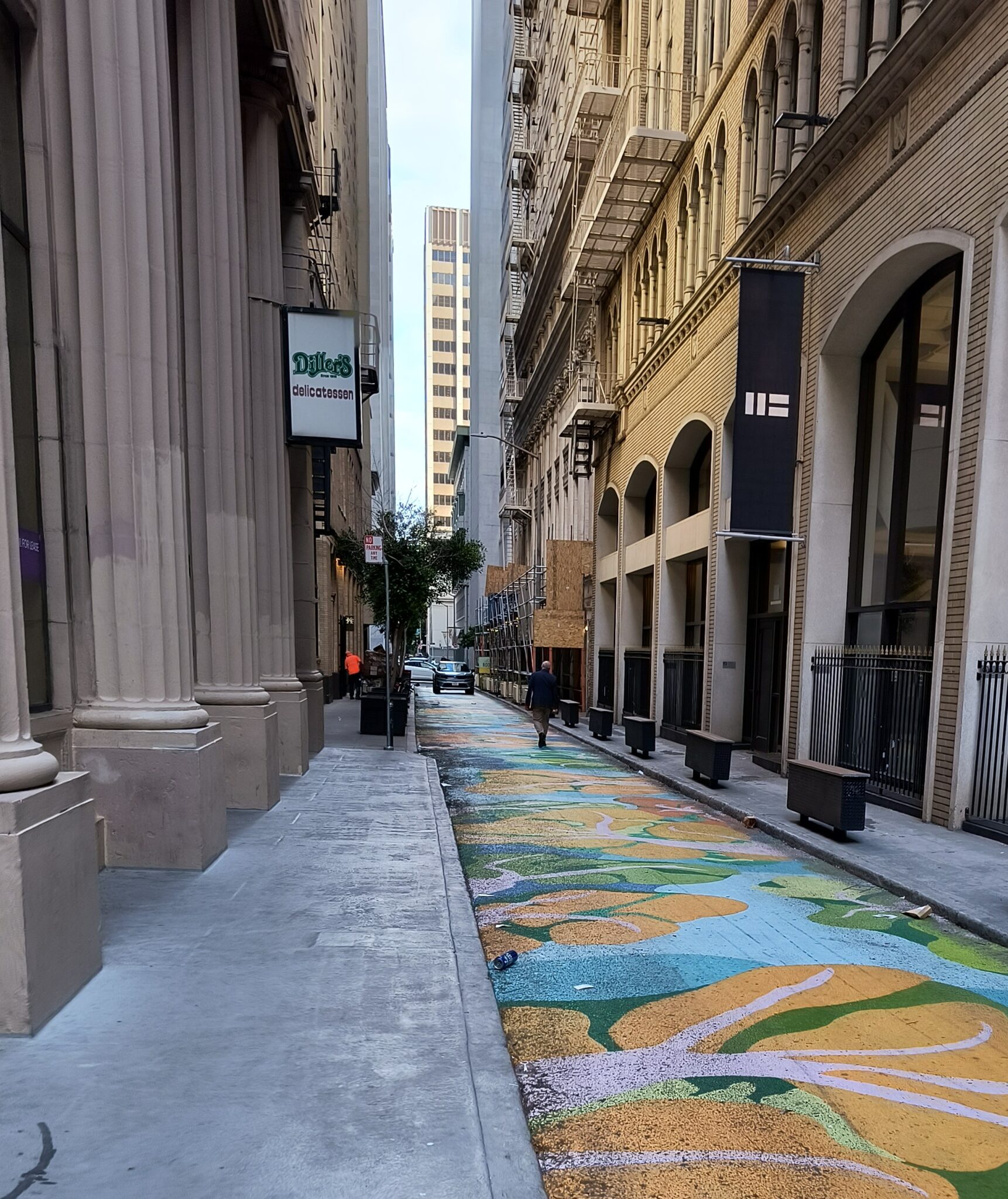 Bright colored blue, green, pink, and orange alley art with benches and businesses nearby