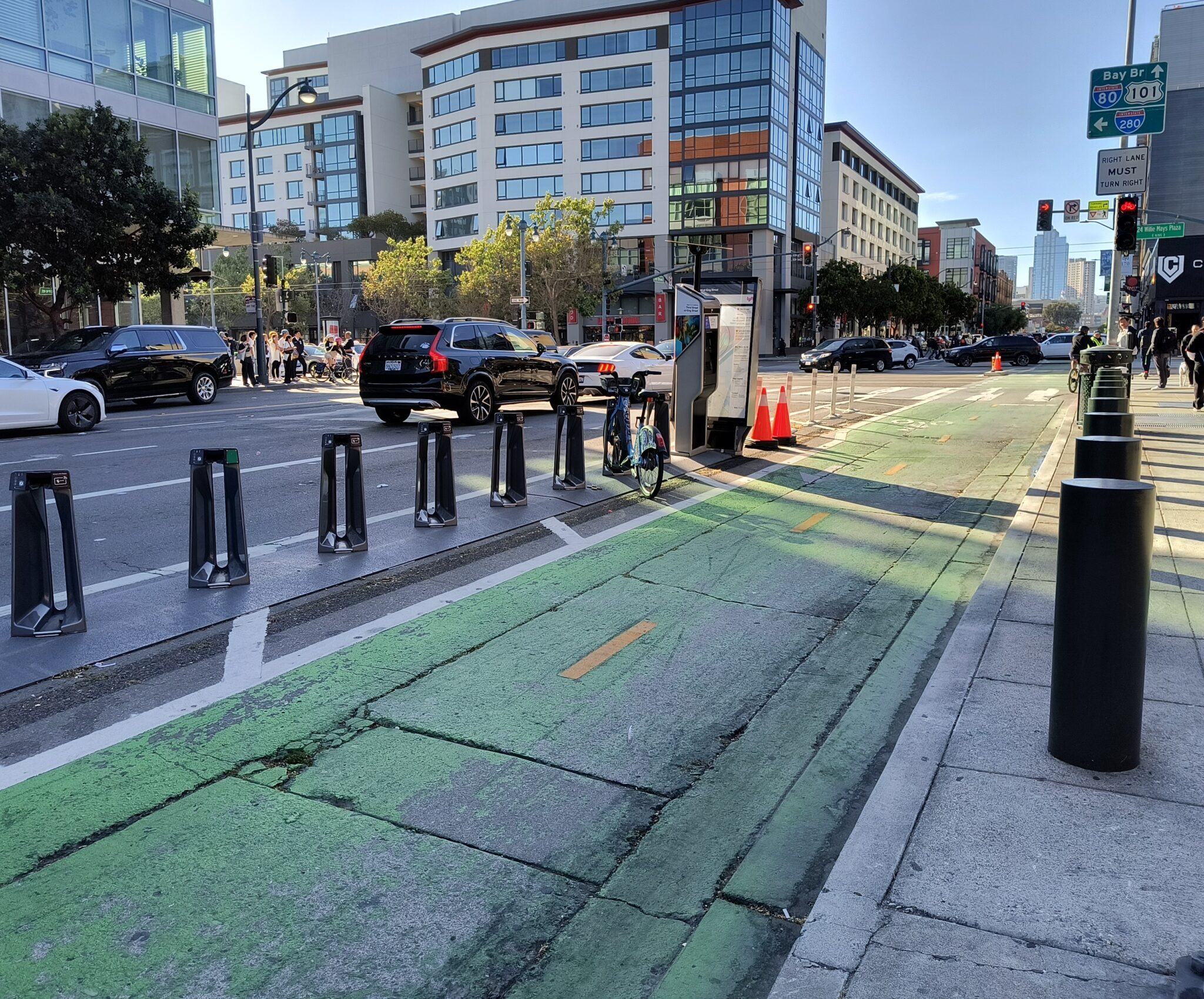 Picture of street with a two-way bike lane in the foreground. Bike chargers are between the bike trail and cars.