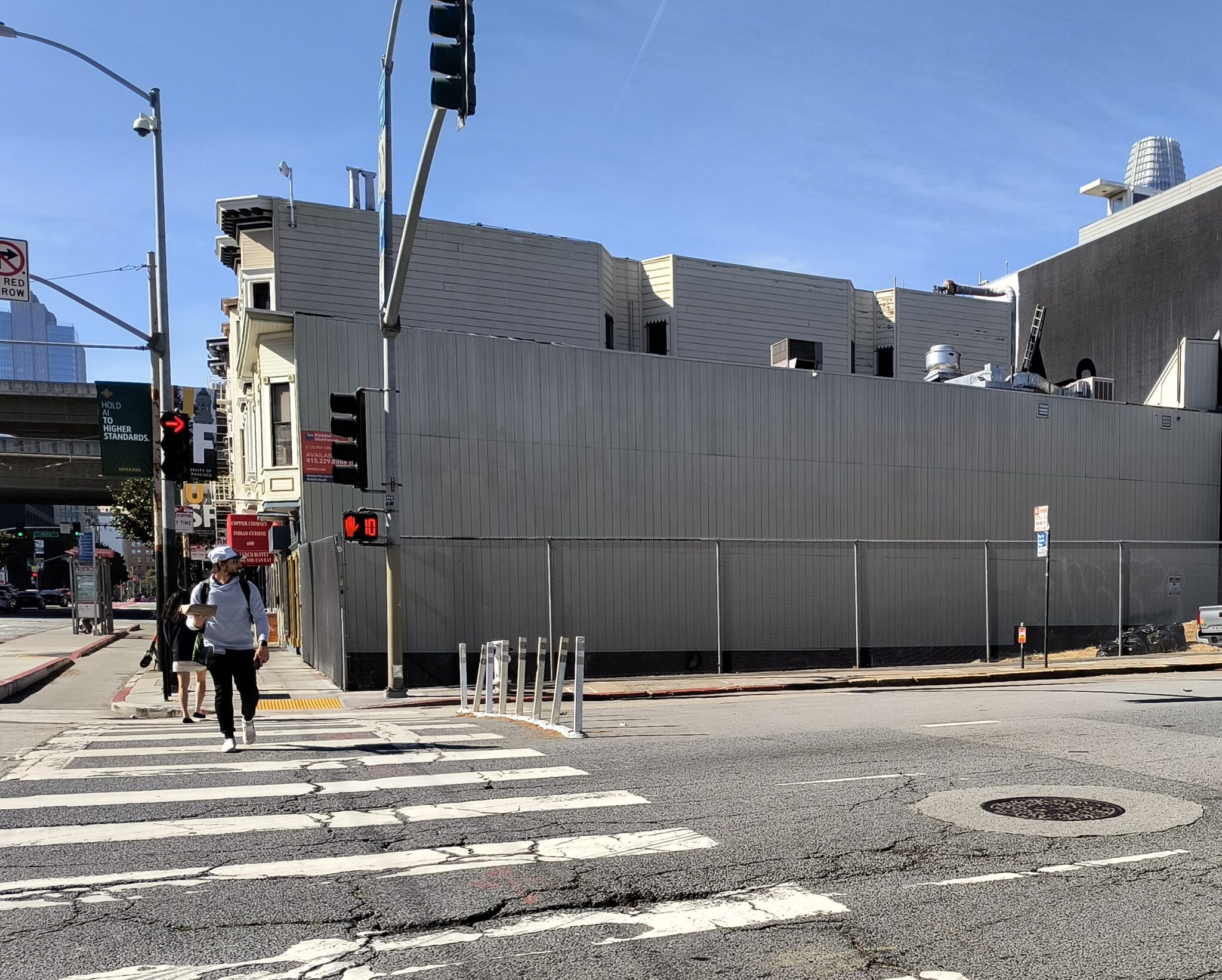 Person walking on a crosswalk with flex posts blocking the left-most lane of the street