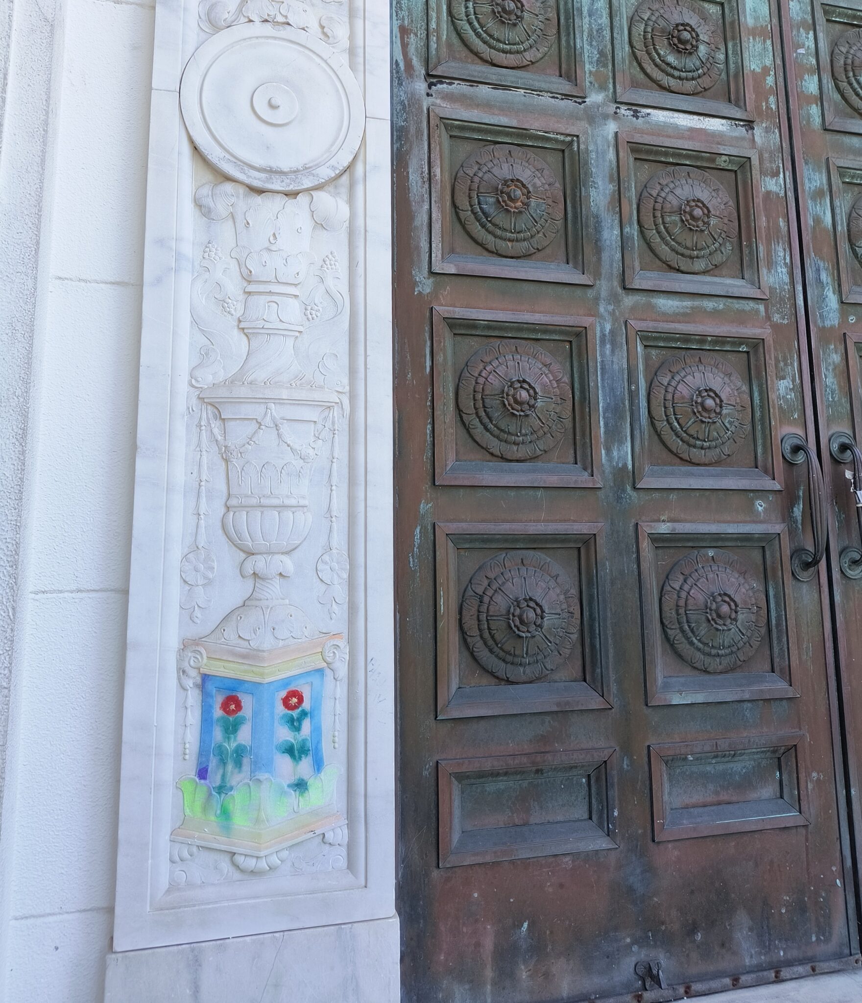 Marble building with tarnished copper doors. One of the bottom designs on the marble has been painted with bright colors